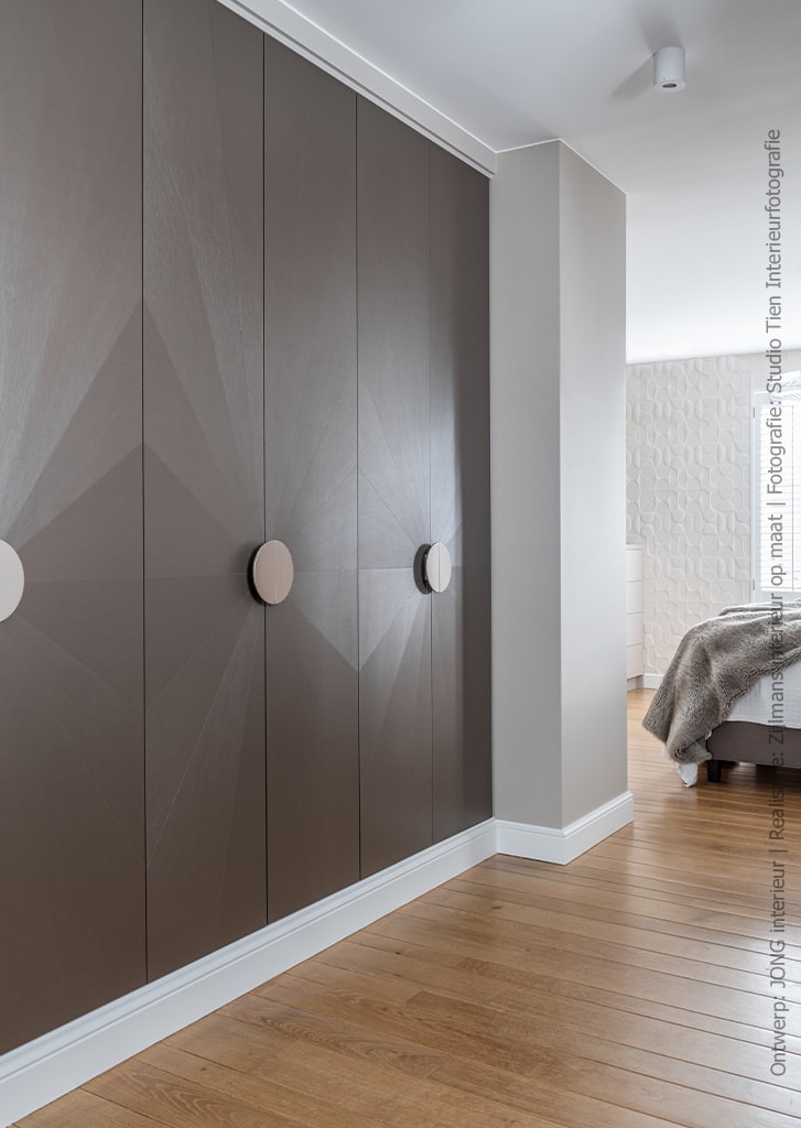 Een stijlvolle maatwerk kastenwand in een slaapkamer gemaakt van decoratief plaatmateriaal van Cleaf. Het plaatmateriaal is in een facetvorm verwerkt waardoor de deuren van de kast er zeer chique uitzien. Decor FA84 Reflex doet denken aan zijdedraad in een warme brons kleur.