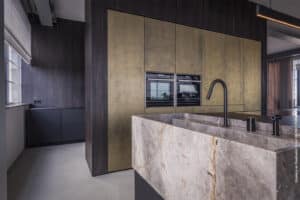 Stoere keuken met granieten werkblad, wasbak en een omlijsting in decoratief plaatmateriaal S012 Yosemite van Cleaf, een gevlamde, donkerbruin decor dat zijn inspiratie vindt in dosse hout