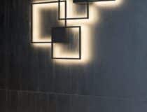 Een zwart wand met decoratieve verlichtingsarmaturen. De wand is afwerkt in zwart plaatmateriaal met een levendige houtstructuur, de U129 Sherwood van Cleaf