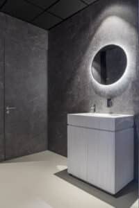 Toilet in de showroom van DecoLegno waarbij de muren zijn uitgevoerd in de FC19 Talco van Cleaf, een donkergrijze marmerlook met ultra matte finish, en het wastafelmeubel in de DM5015 Luna van Durasein, met een vloeiend lijnenspel in een serene, witte kleurmelange