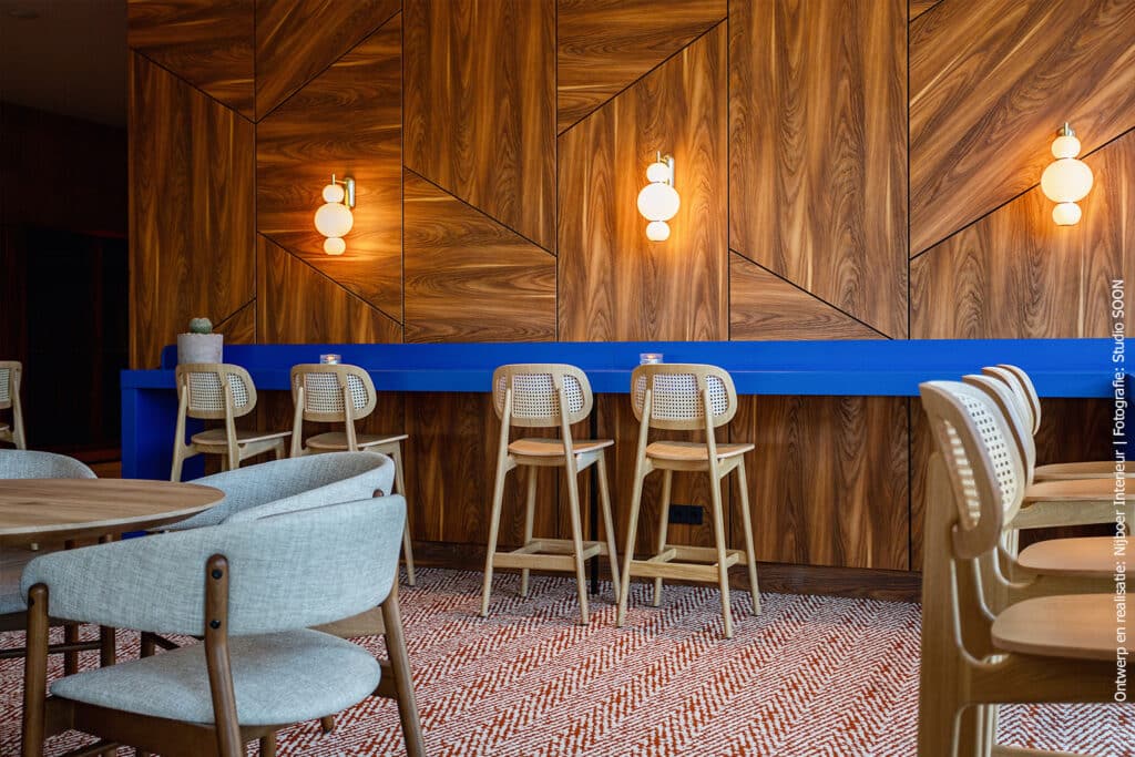 Wandafwerking in een restaurant met panelen waardoor een grafisch lijnenspel ontstaat. De wand is afgewerkt met decoratief plaatmateriaal met een warm houtdecor, De S016 Yosemite van Cleaf.