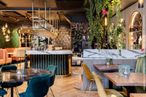 Kleurrijk restaurant met een verfijnde mamerlook op de tafelbladen, aan de bar en op de bartafels door decoratief plaatmateriaal FB38 Talco van Cleaf, welke een uitstraling van Carrara marmer in wit met donkergrijze aders heeft.