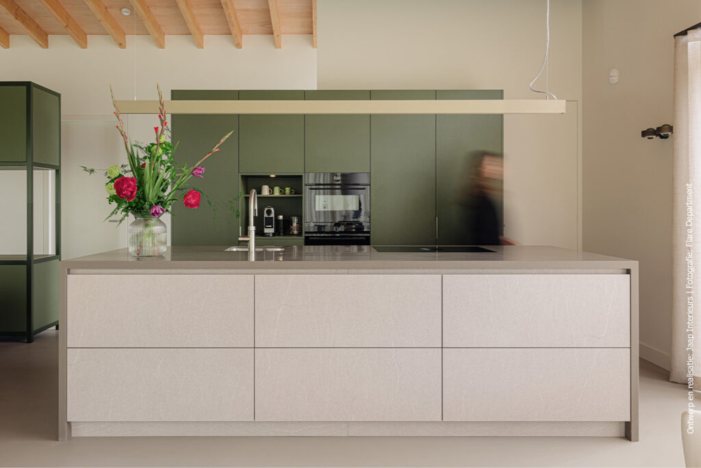 Deze moderne keuken combineert legergroene keukenkasten in de UB54 Primofiore van Cleaf met een kookeiland ontworpen in de cementlook van de FC36 Concreta van Cleaf, en een blad in de kleikleur DM2034 Adrift van Durasein®